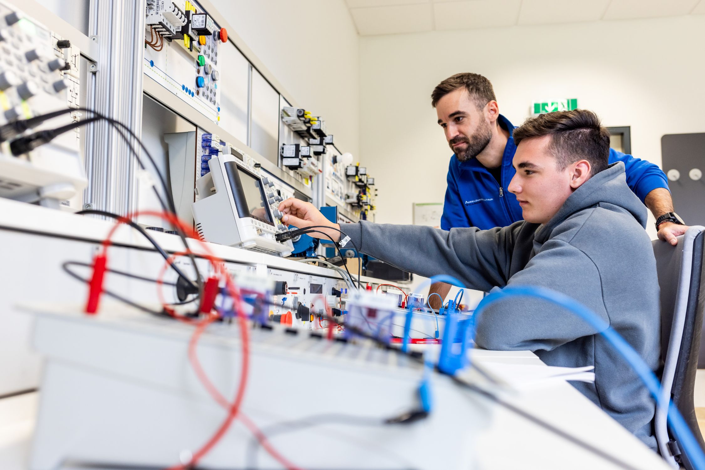 Betreuer zeigt Lehrling die Bedienung von Geräten